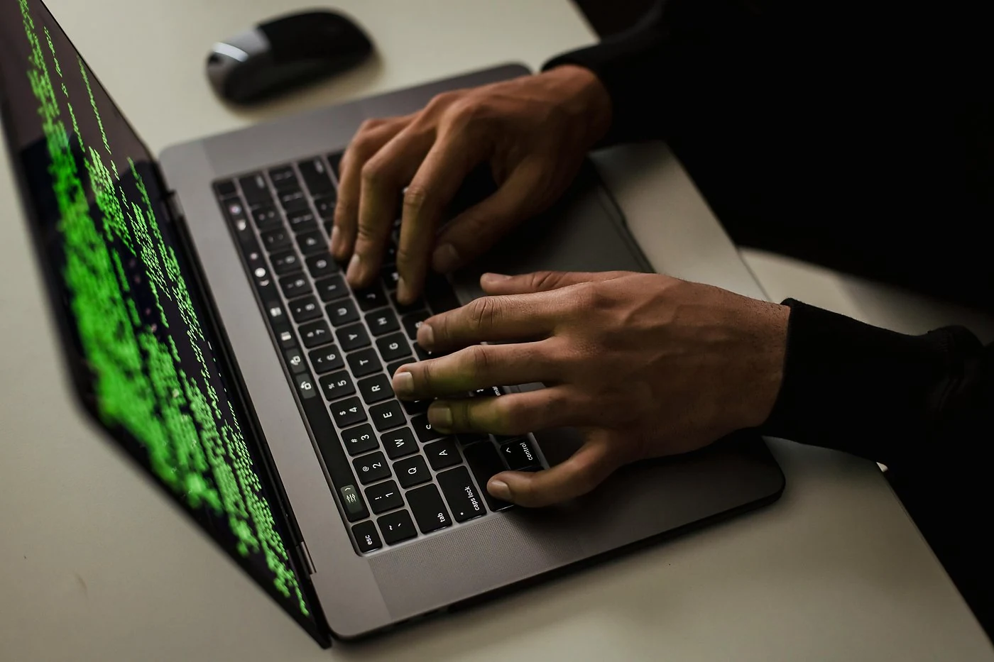 Persoon typt op laptop met groene code op het scherm, illustratie van een cyberaanval