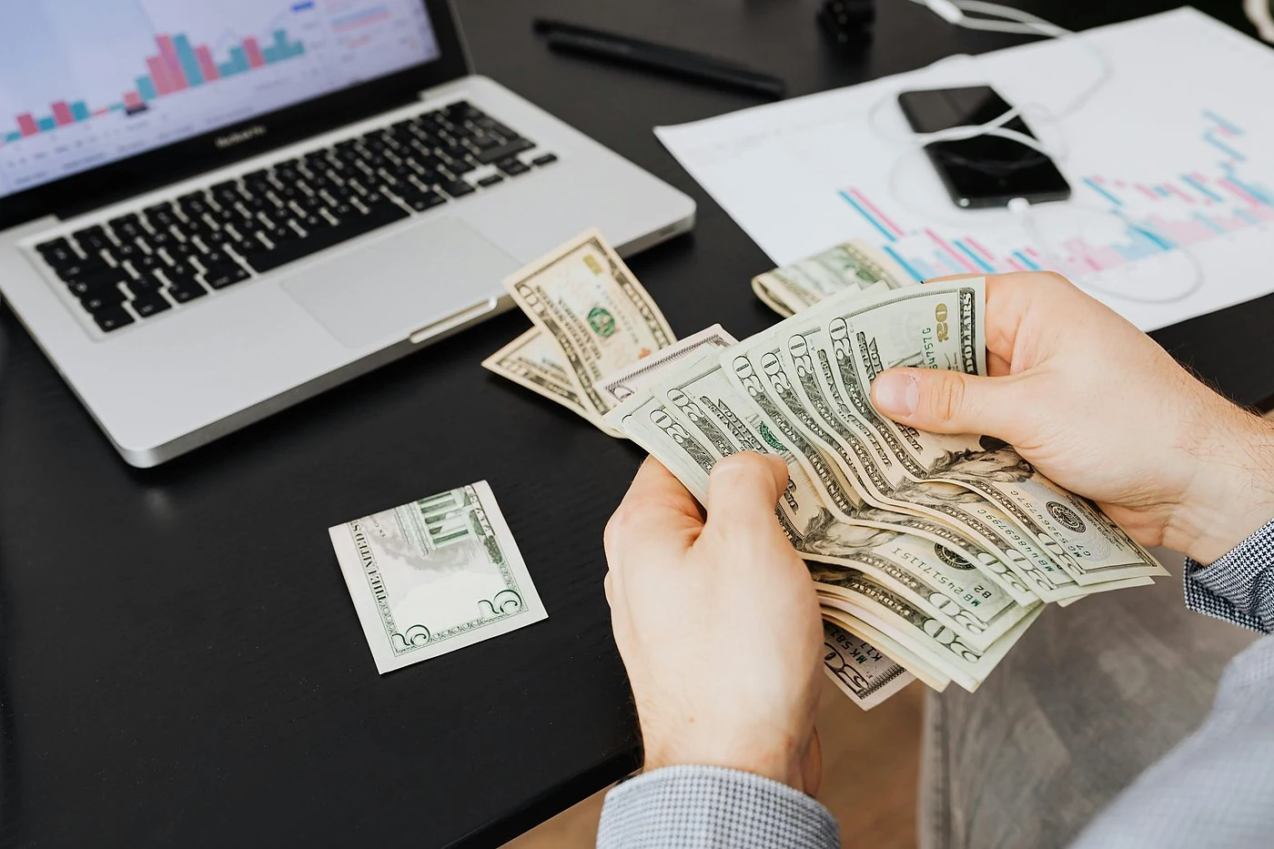 Handen tellen bankbiljetten voor laptop met financiele grafieken, illustratie van de kosten van een ransomware aanval